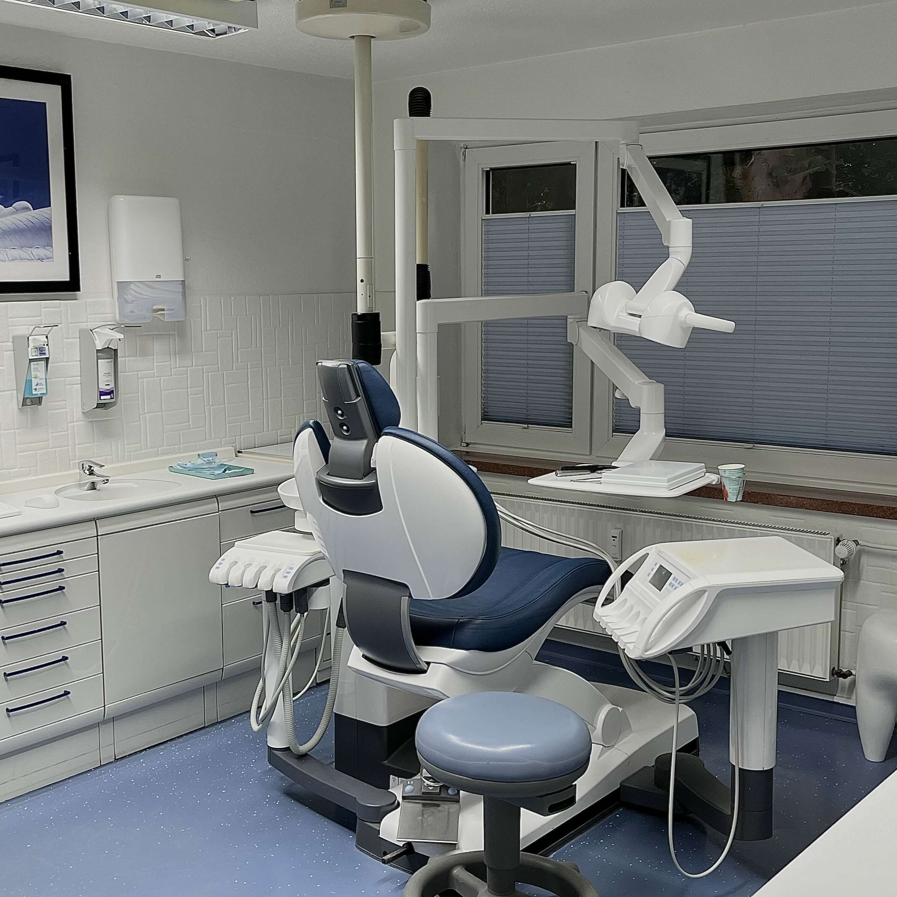 A dentist in a white coat and mask stands next to a patient who is seated and working on a laptop. The background includes a large screen displaying a tooth graphic and a calendar, along with a wall clock. Potted plants are placed on either side, contributing to a calm and welcoming office environment.